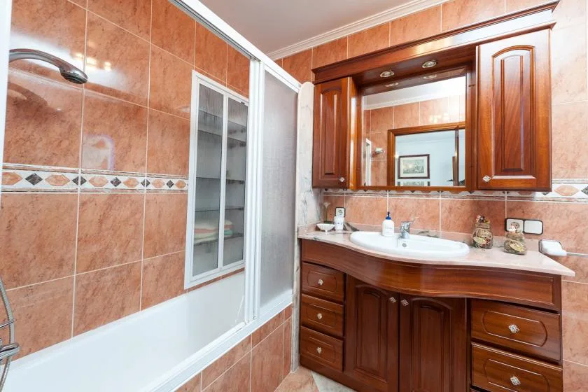 A tiled bathroom with a bathtub, sink, and wooden vanity.