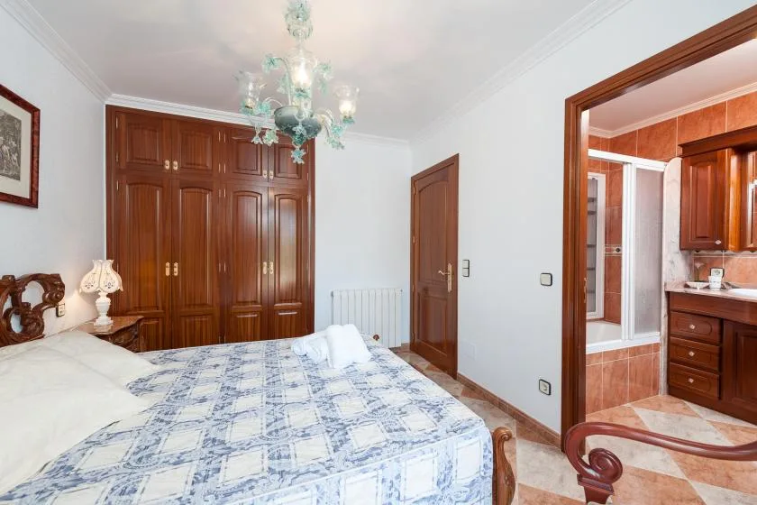 A bedroom with a patterned bedspread, wooden wardrobes, and an adjoining bathroom.