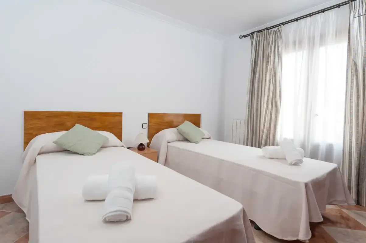 A bright bedroom with two beds and towels folded on the bedding.
