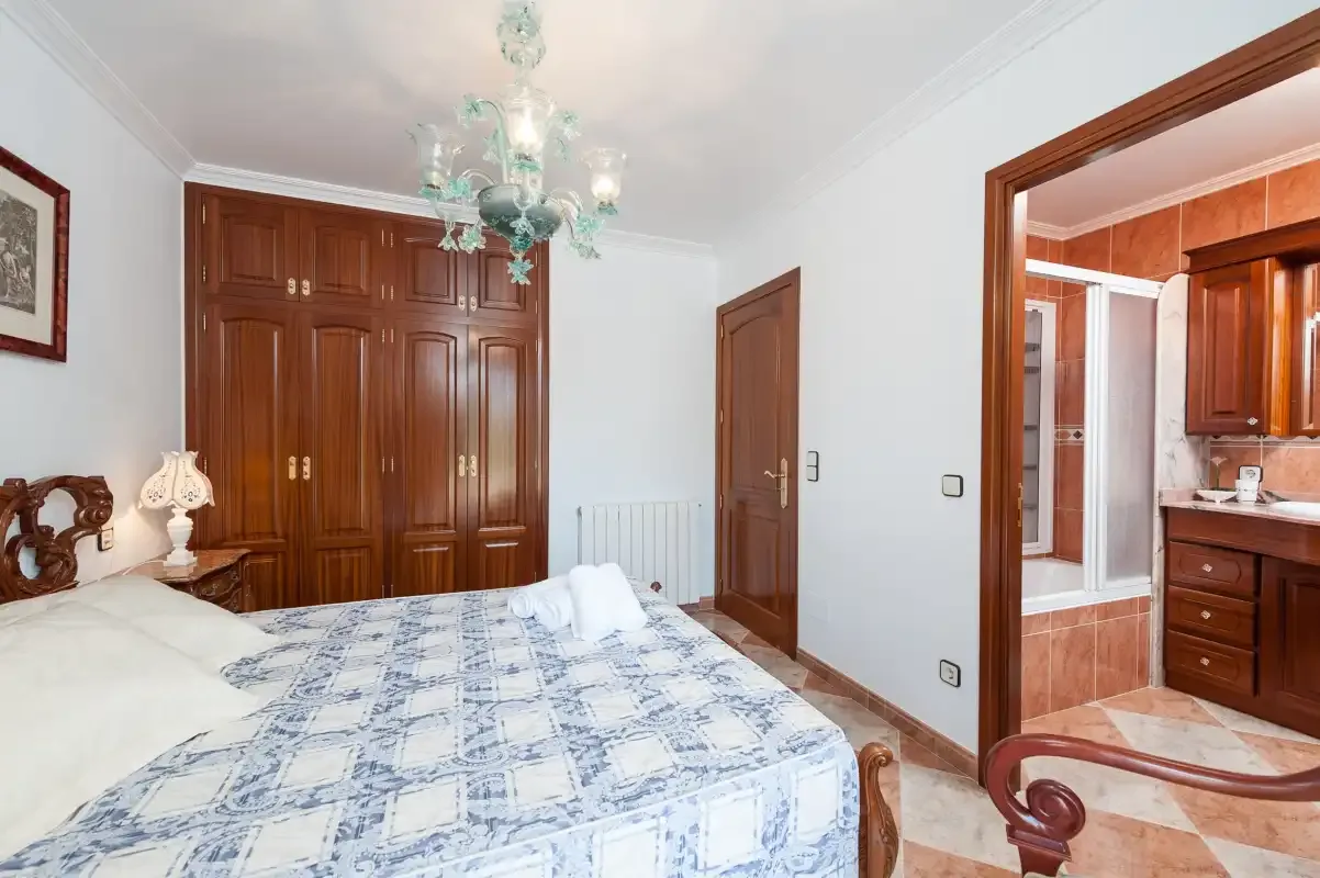 A bedroom with a patterned bedspread and an open doorway to a tiled bathroom.
