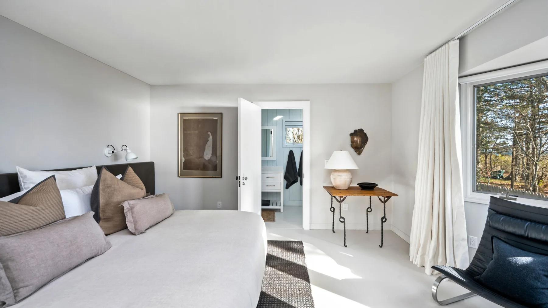 Un dormitorio luminoso con una cama, una mesa pequeña y una ventana grande.