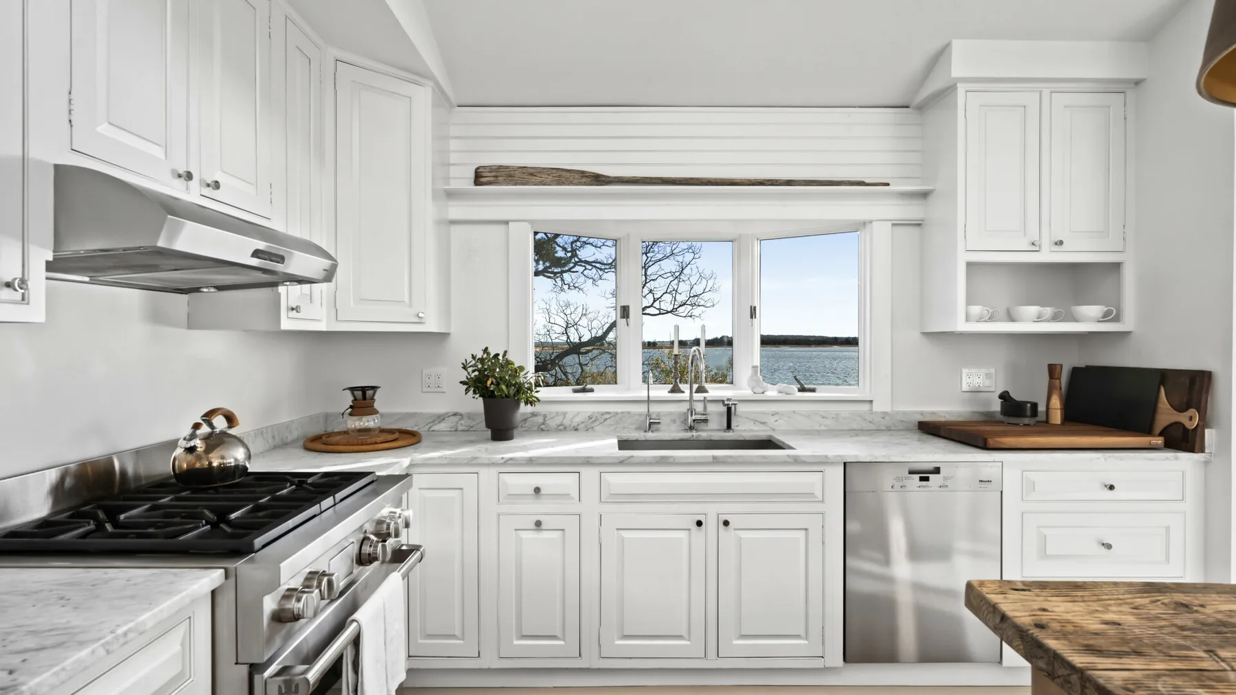 Una cocina blanca y luminosa con una ventana amplia frente al agua.