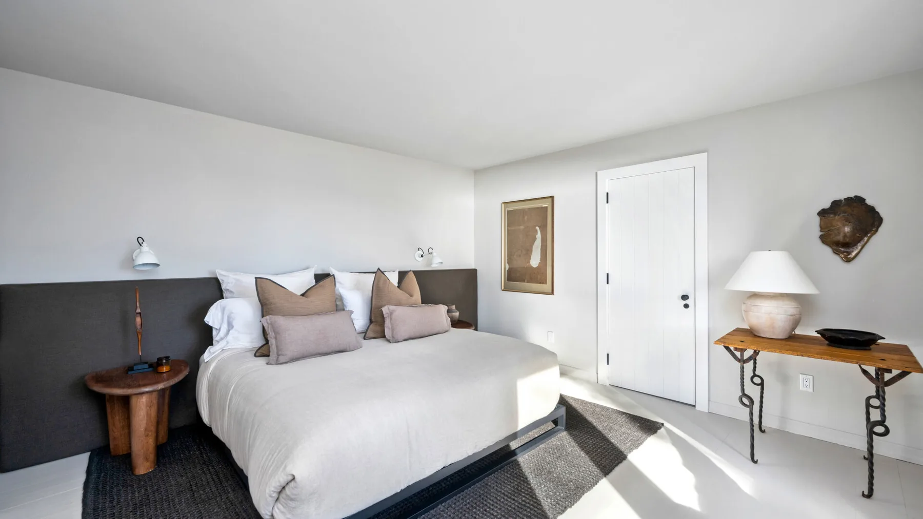 Un dormitorio luminoso con una cama tendida y una mesita a un lado.