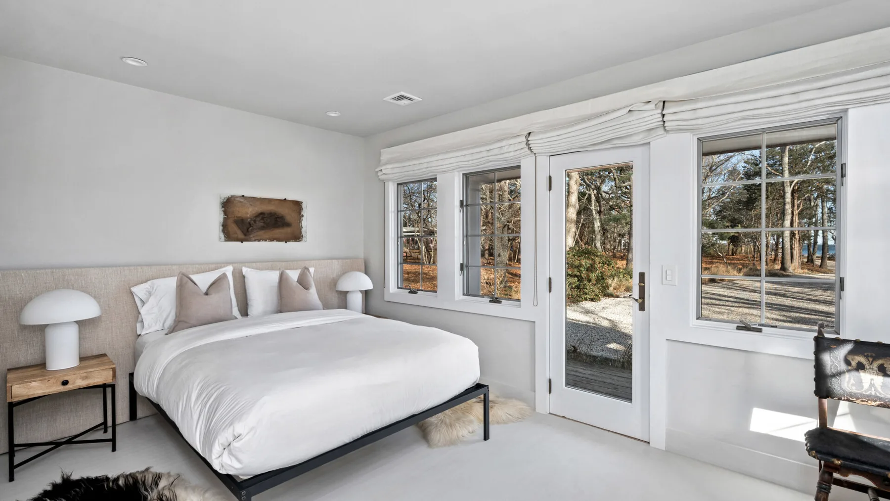 Un dormitorio luminoso con una cama bien arreglada junto a grandes ventanas y una puerta de vidrio.