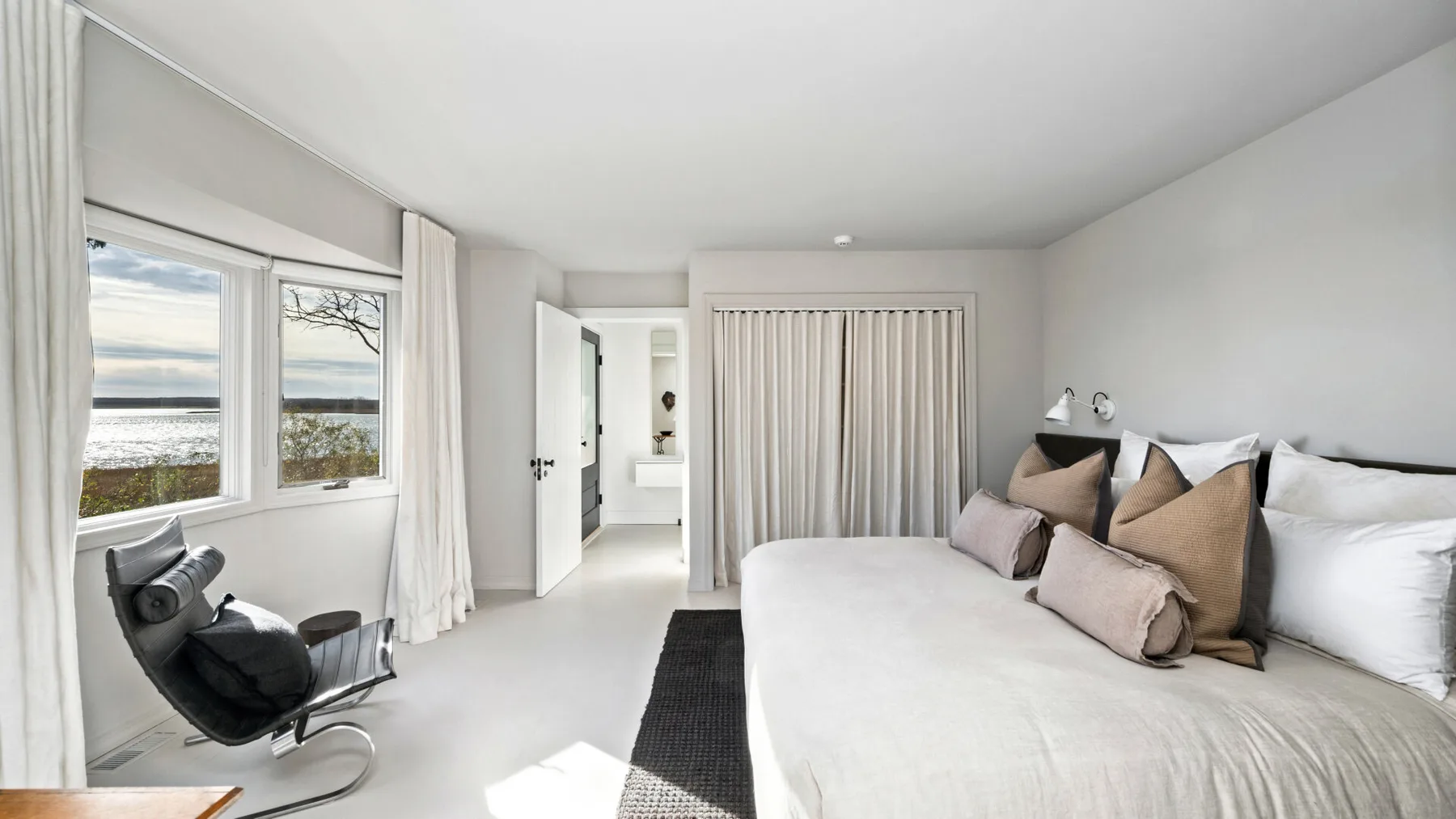 Un dormitorio luminoso con una cama grande, una ventana con cortinas y asientos.