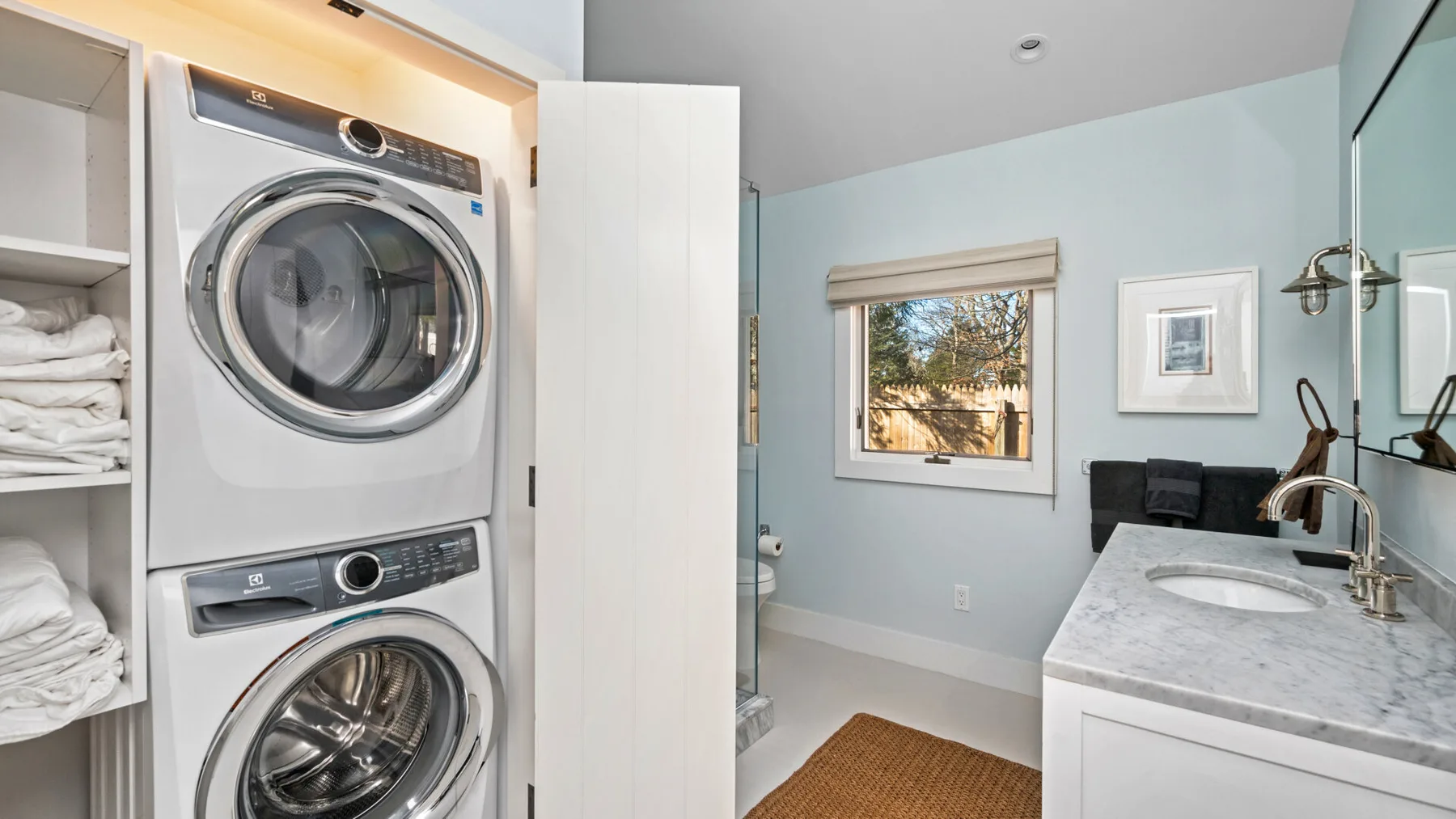 Zona de lavandería con máquinas apiladas junto a un lavabo de baño y una ventana.
