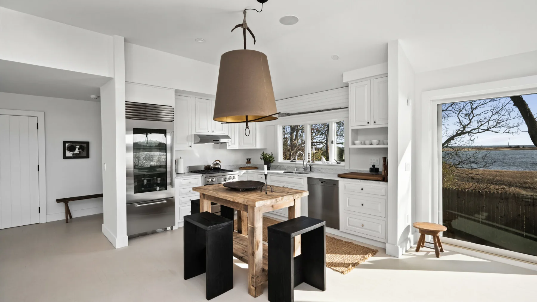 Una cocina luminosa con una gran isla de madera y asientos oscuros.