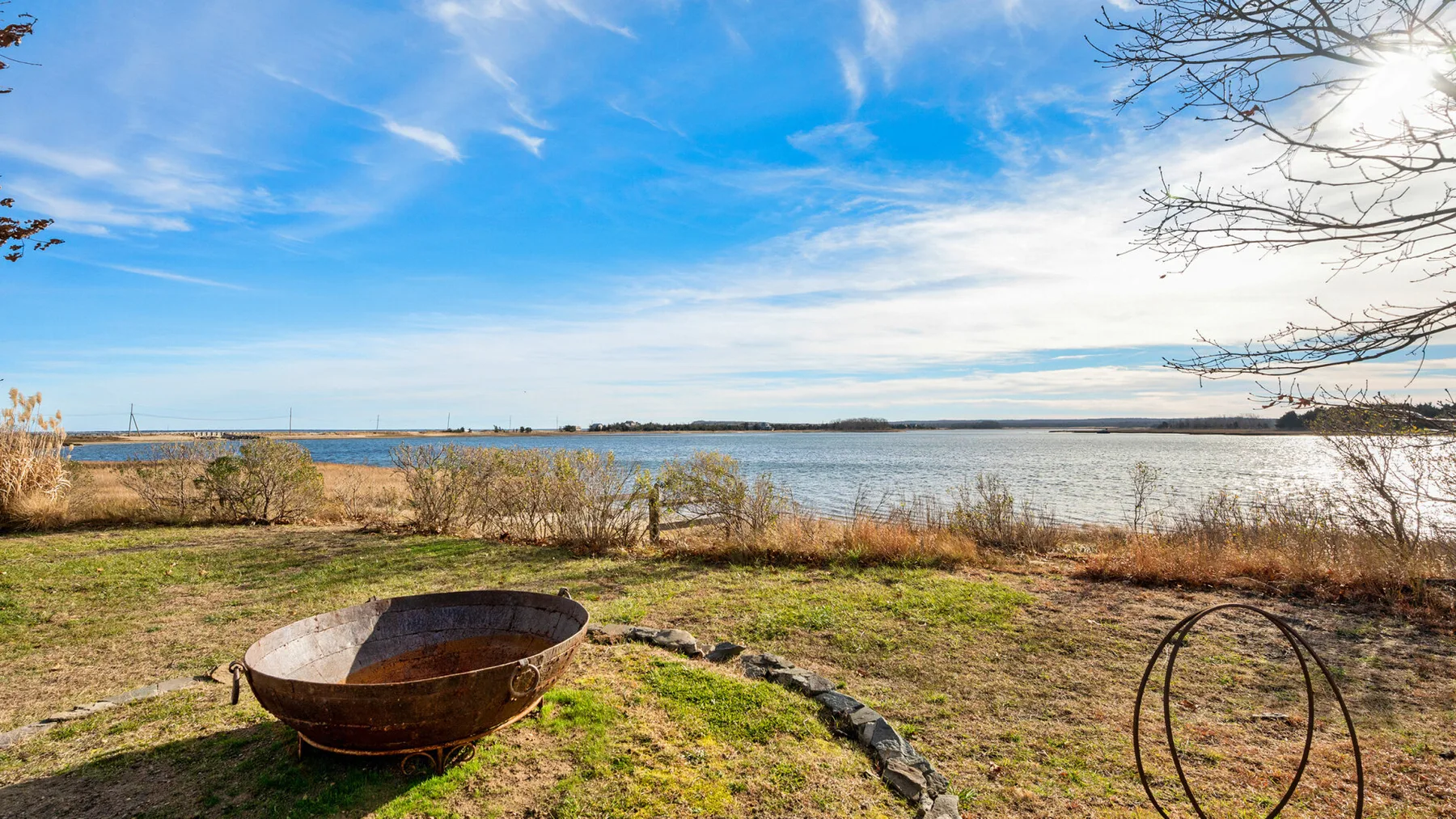 Un patio junto al lago con césped y un pequeño brasero metálico junto al agua.