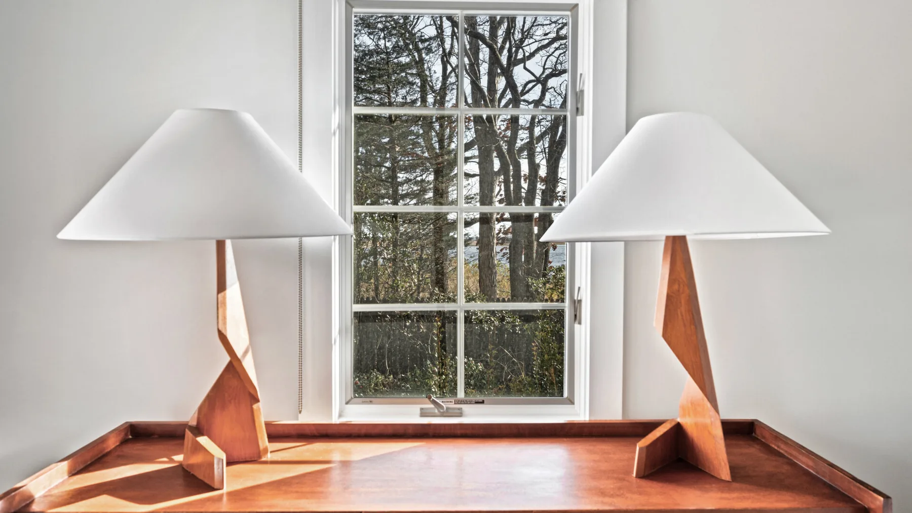 Una ventana luminosa con dos lámparas escultóricas sobre un alféizar de madera.