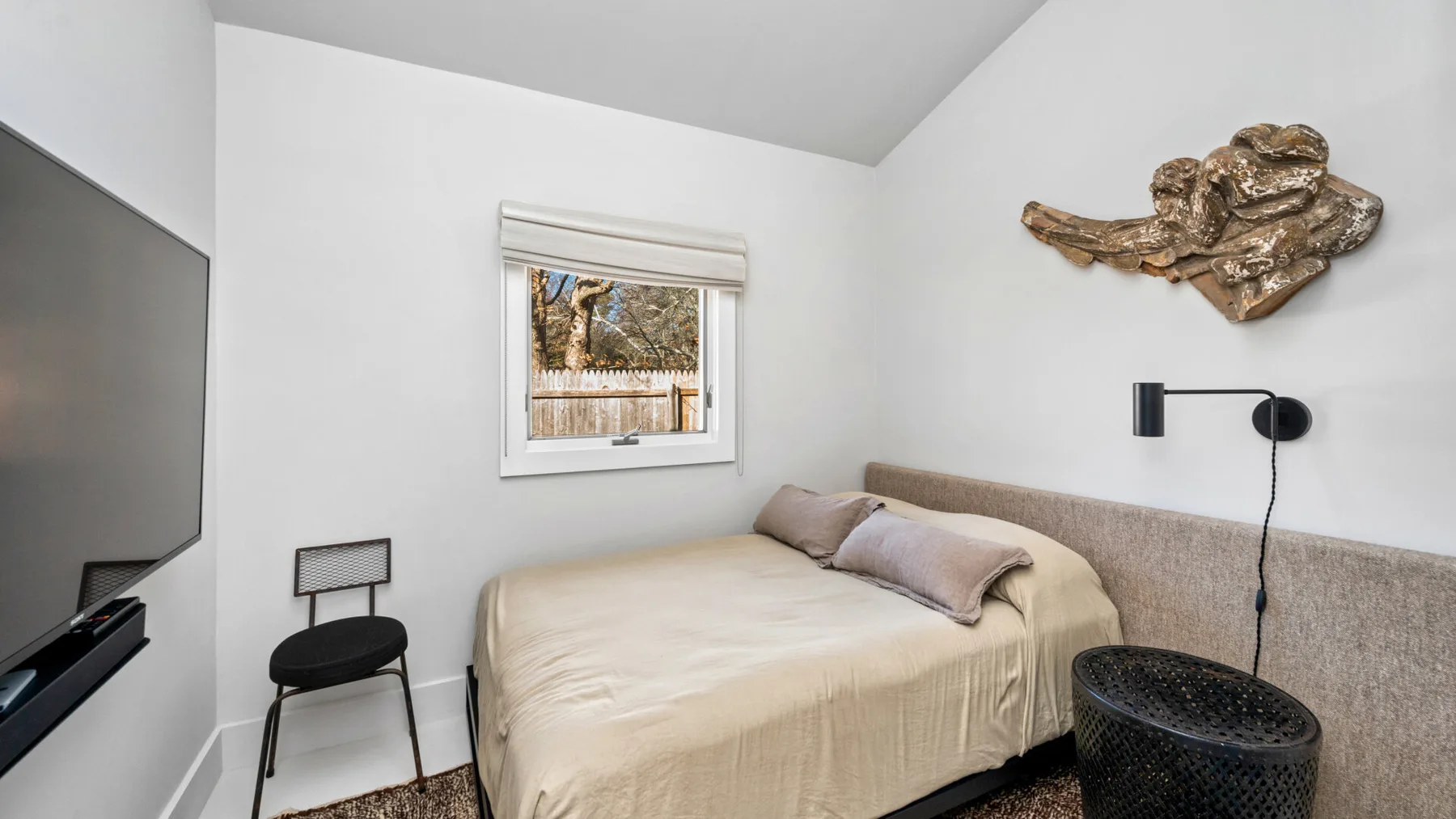 Un dormitorio con una cama, un televisor en la pared y una ventana pequeña.