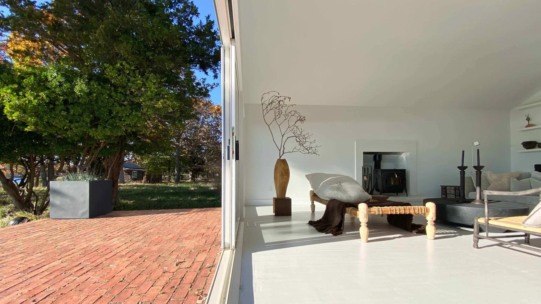 Una sala luminosa se abre a un patio de ladrillo y un jardín frondoso.