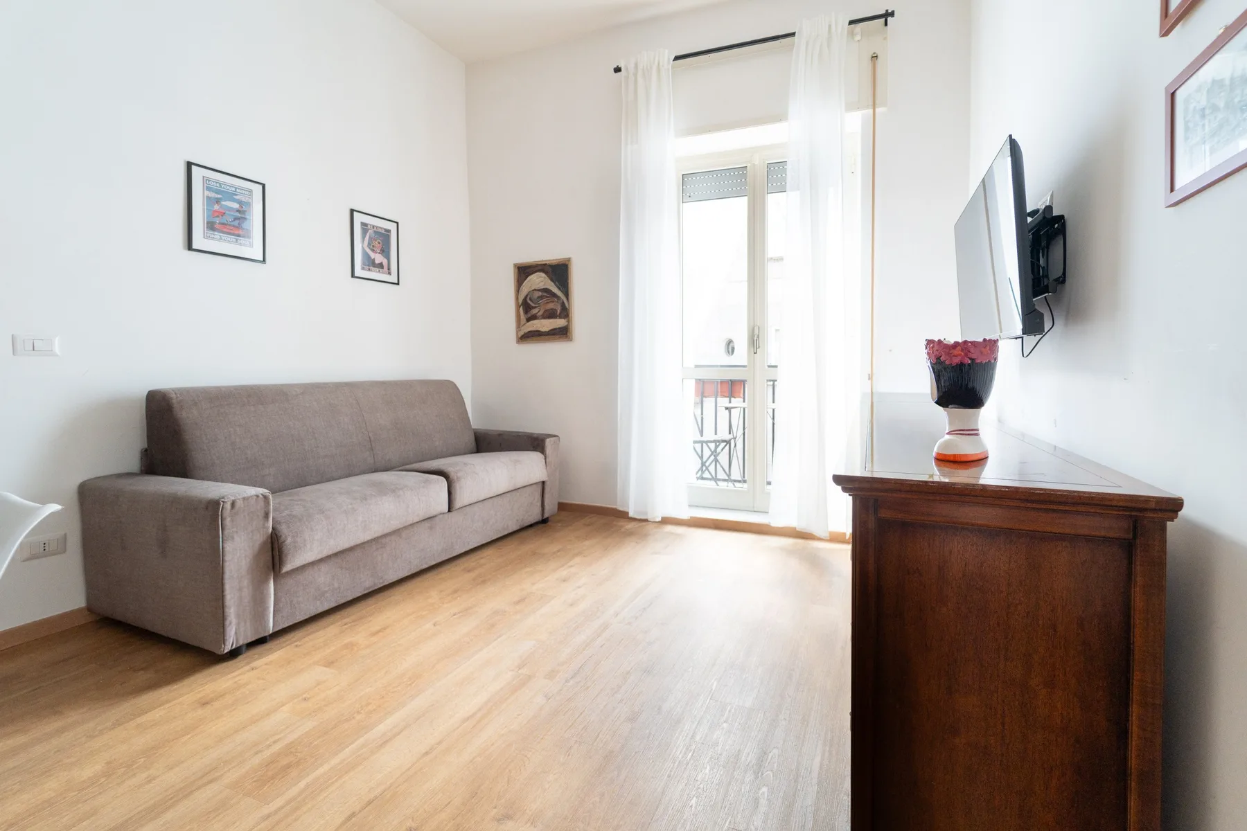 A bright living room with seating, a television, and a glass door opening to a small balcony.