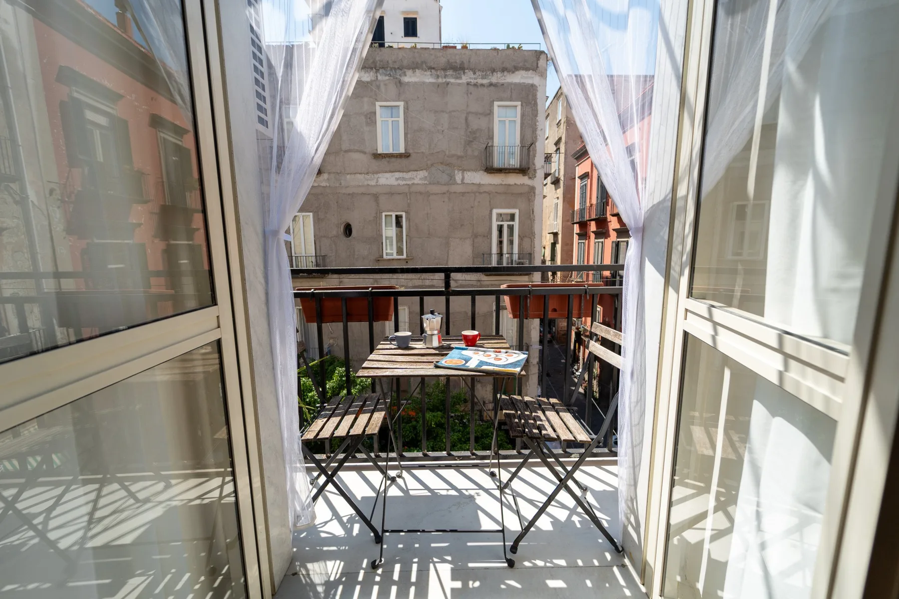 A small balcony with a table and chairs is framed by open glass doors.
