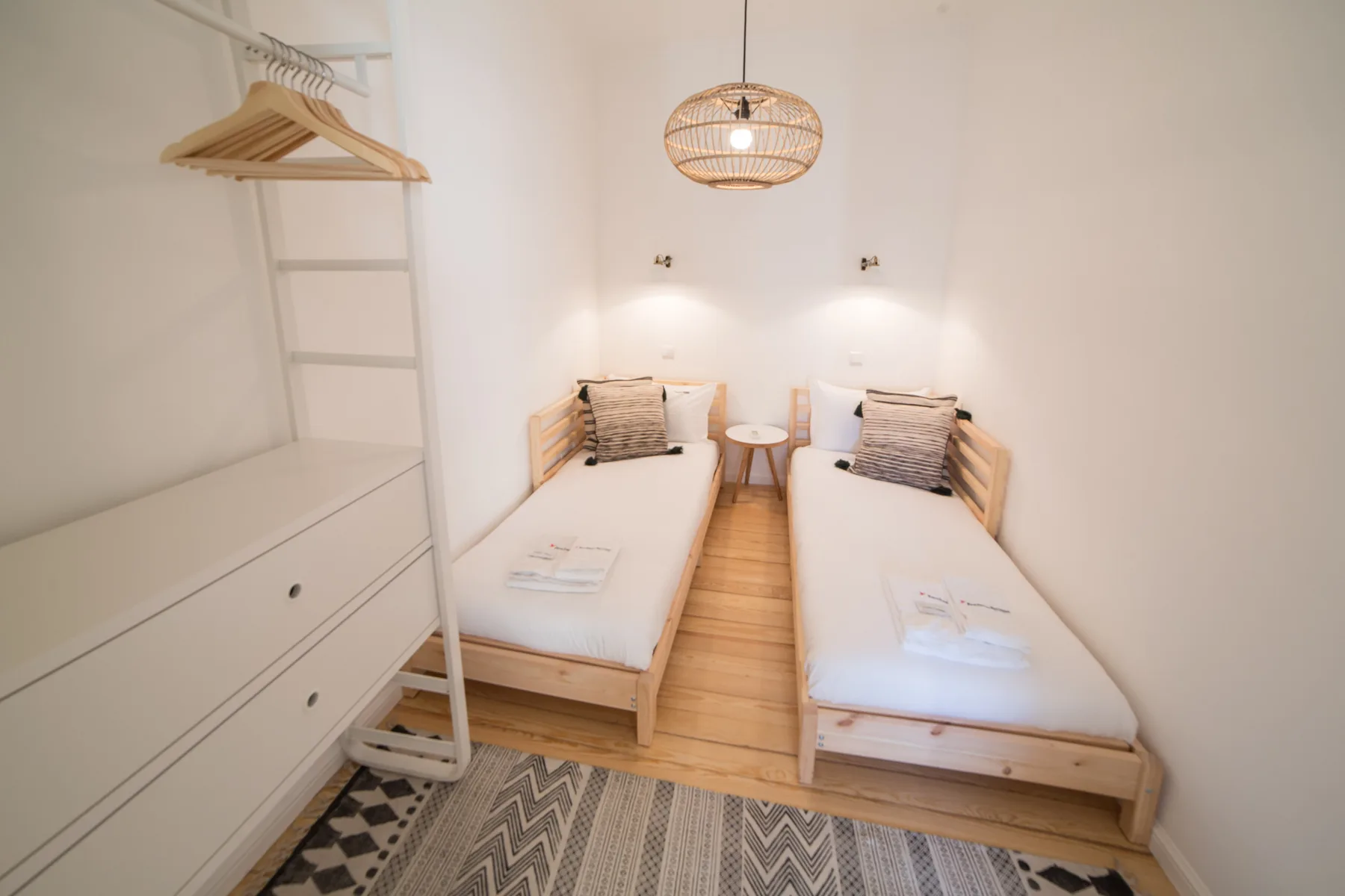 A bright twin bedroom with two single beds and a hanging pendant light.
