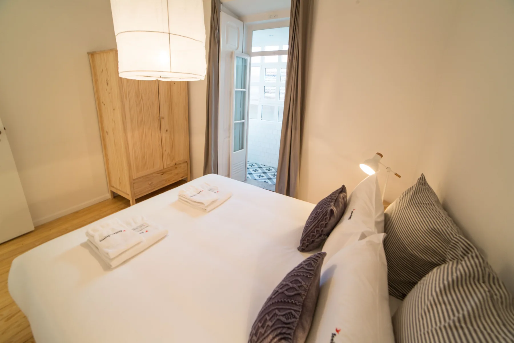 A bedroom with a neatly made bed and a wooden wardrobe beside the doorway.