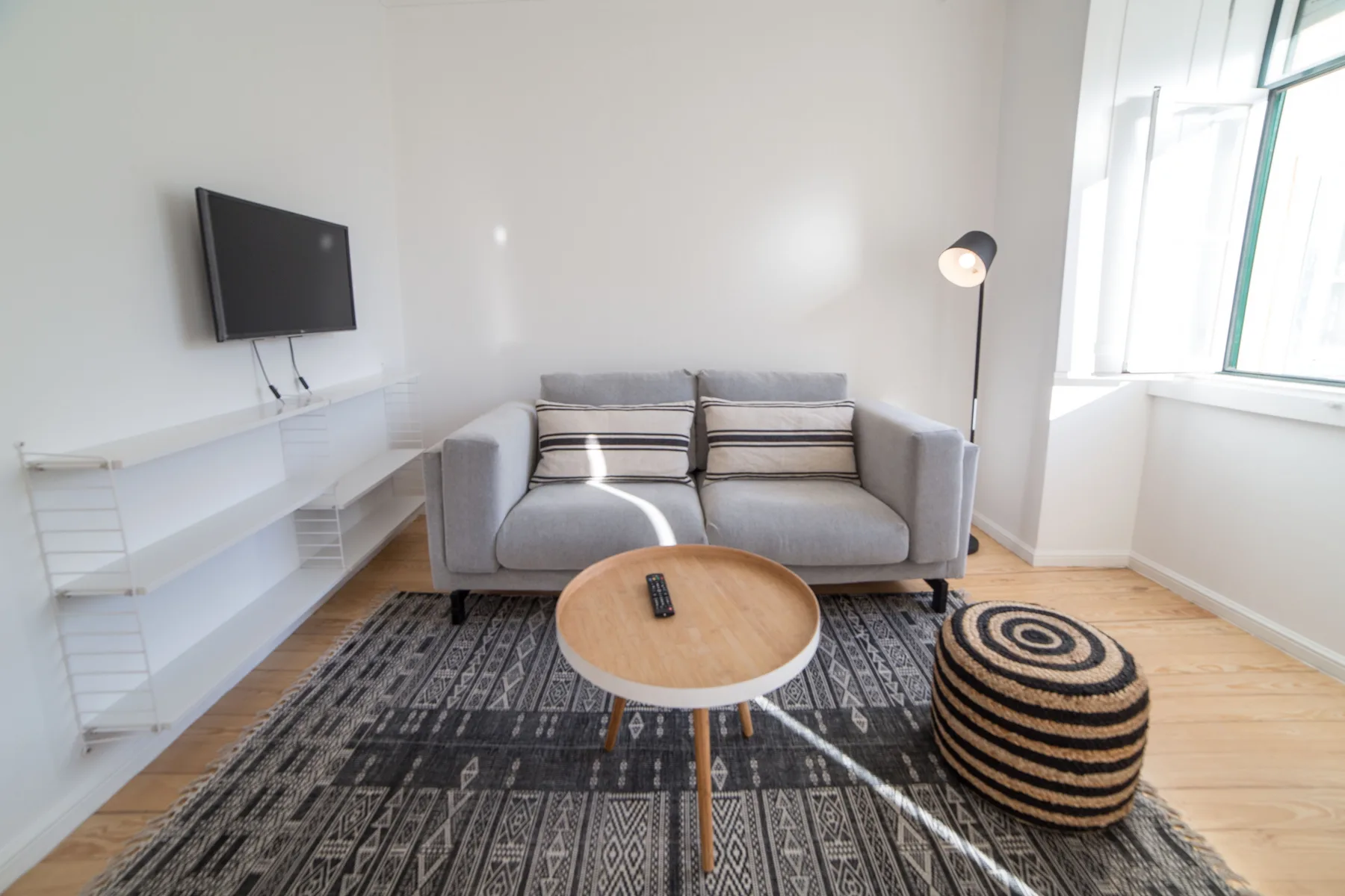 A bright living room with gray seating, a patterned rug, and a round coffee table.