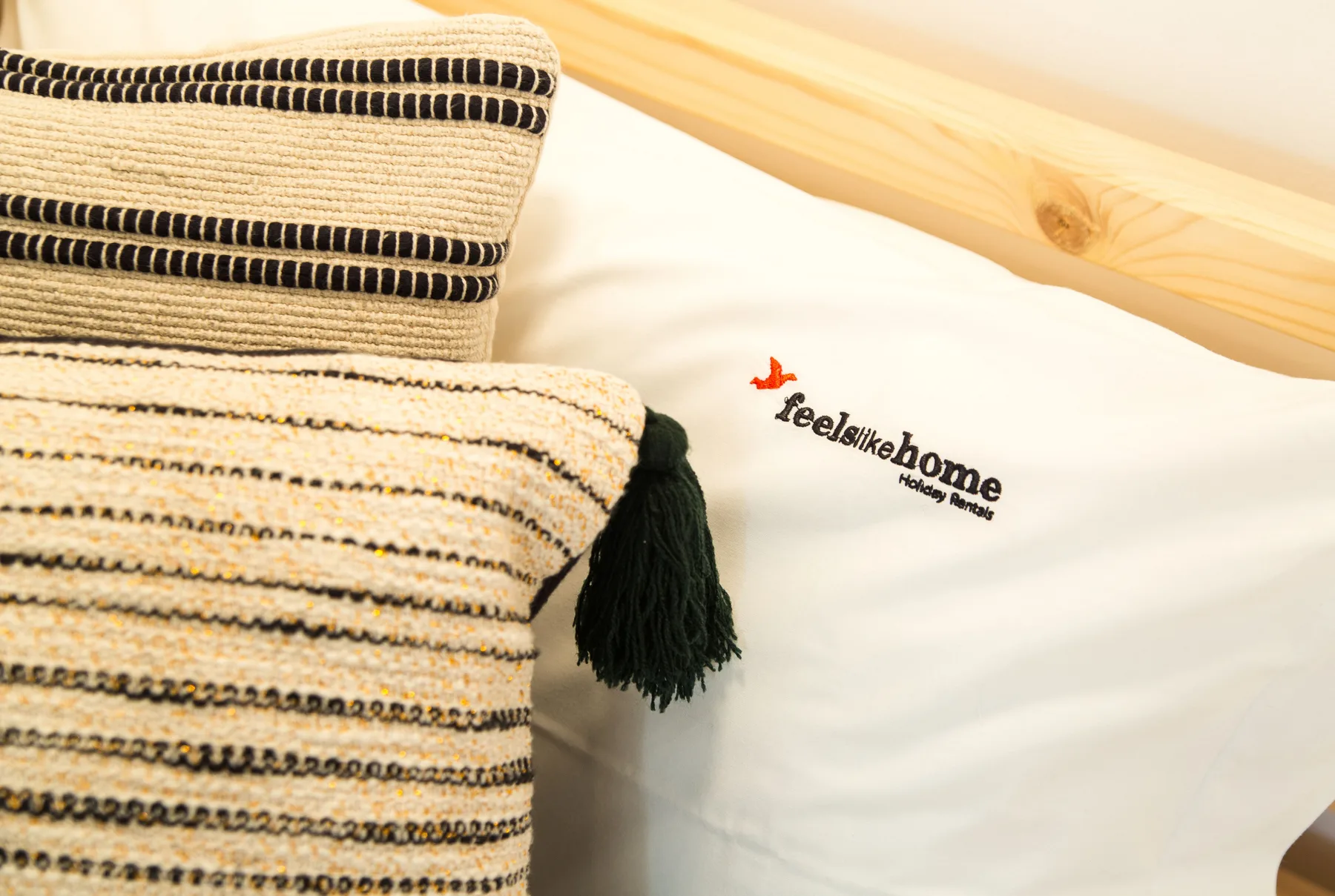 Folded patterned textiles rest on a white bed beside a wooden headboard.