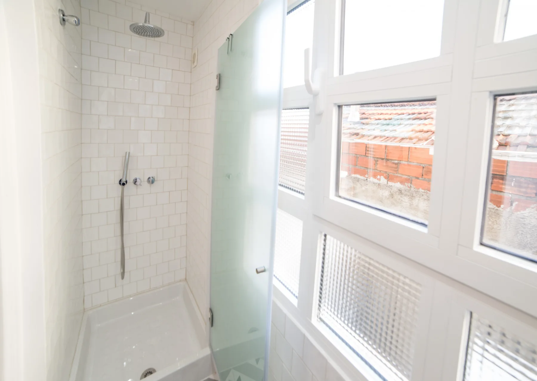 A bright tiled bathroom with a shower and large windows.