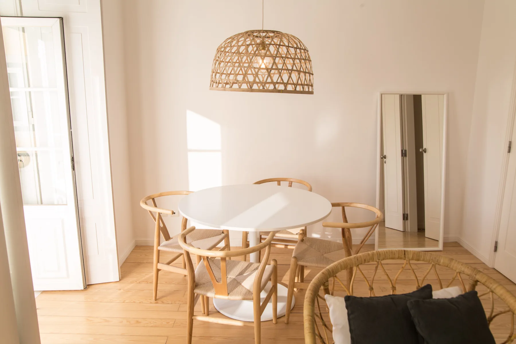 A bright dining area with a round table and woven pendant lamp.