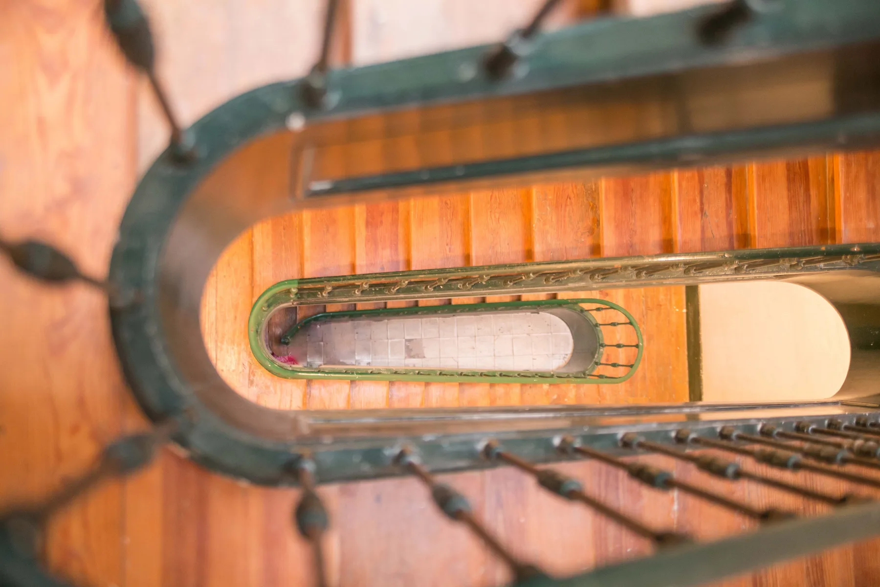 A view down a wooden spiral staircase with dark metal railings.