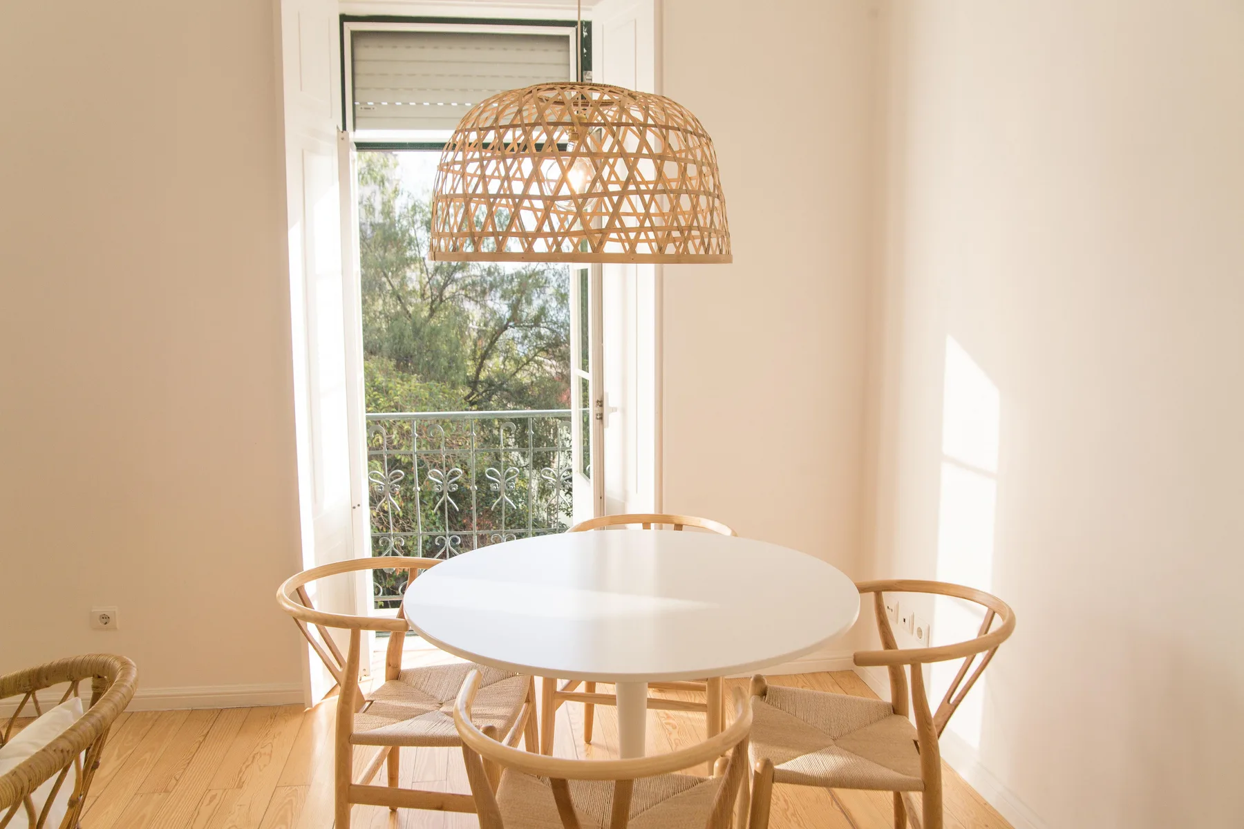 A bright dining area with a round table and woven pendant light by the window.