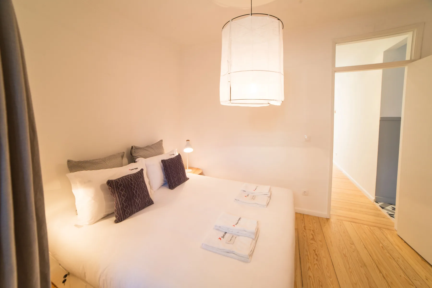 A bright bedroom with a neatly made bed and an open doorway.