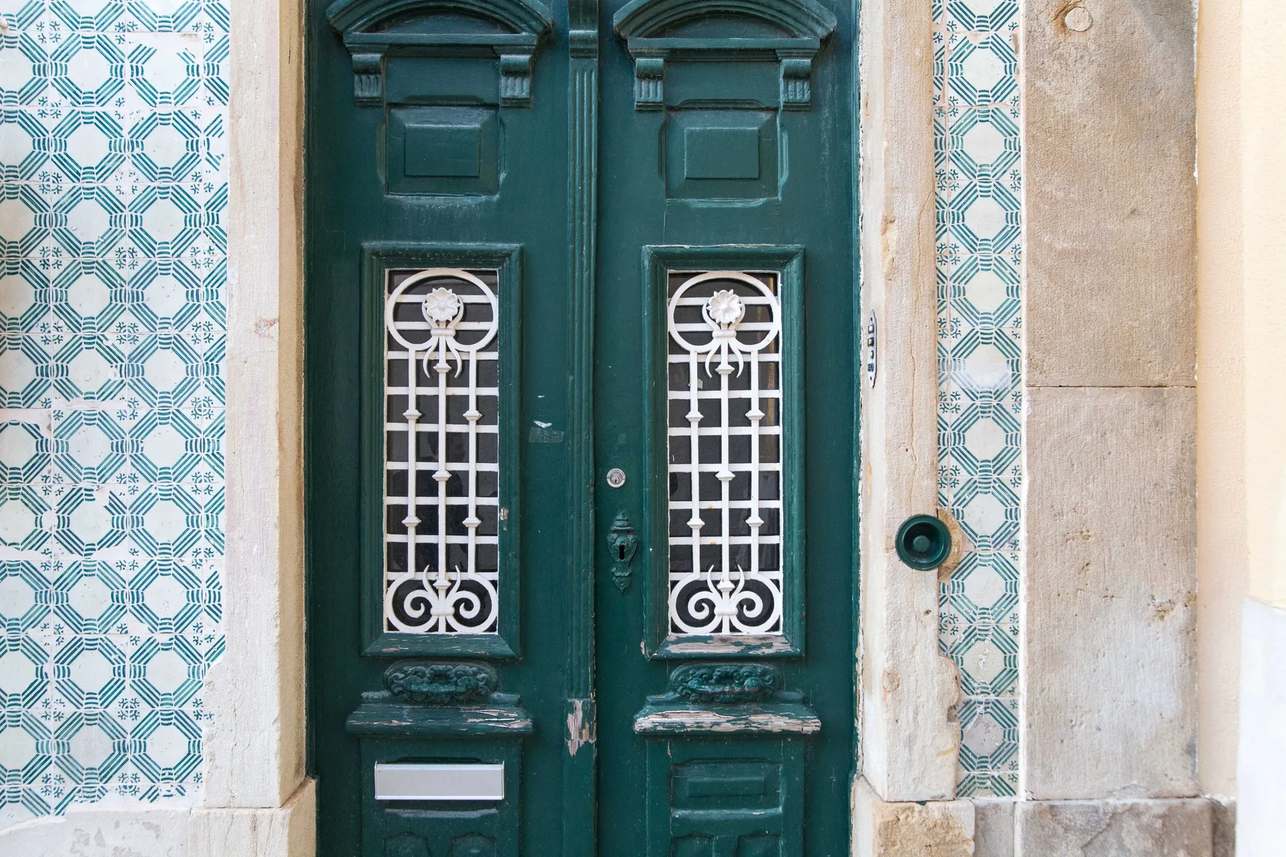 A dark green double door with decorative white grilles and patterned tile surrounds.