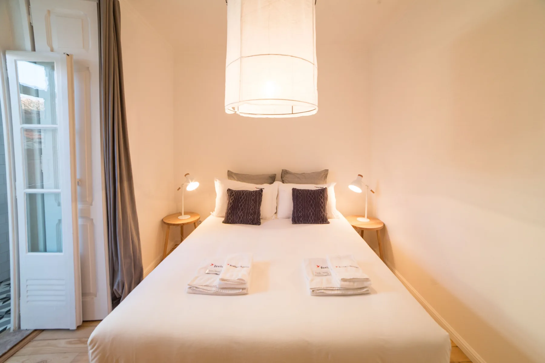 A bright bedroom with a bed, bedside tables, and a hanging light.
