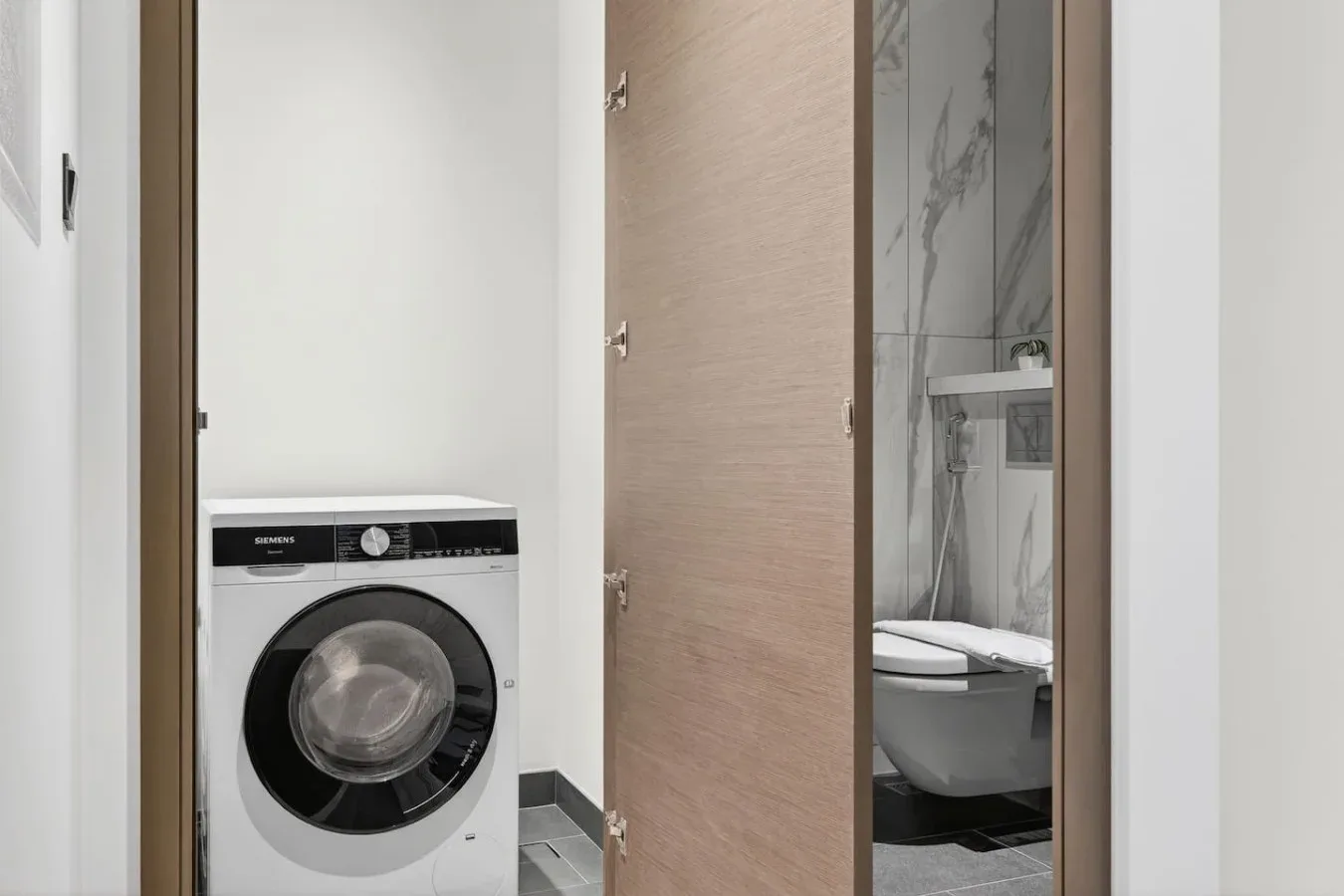 Un baño con una lavadora de carga frontal junto a una ducha.