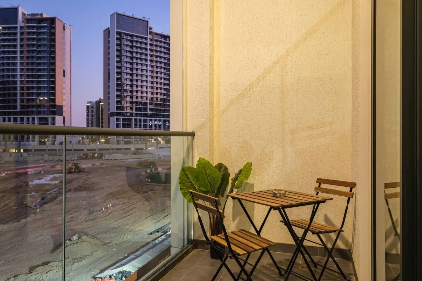 Un balcón con una mesa pequeña y asientos da a edificios altos cercanos.