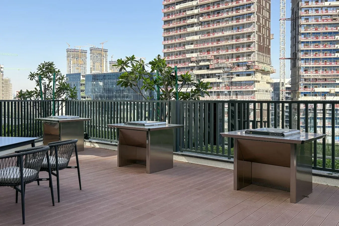 Una terraza exterior tiene varias mesas junto a una barandilla oscura, con edificios de la ciudad al fondo.