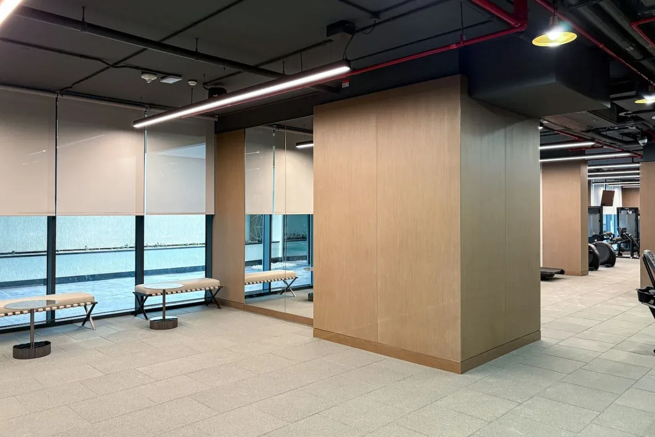 Interior de gimnasio moderno con equipo de ejercicio y bancos junto a grandes ventanas.