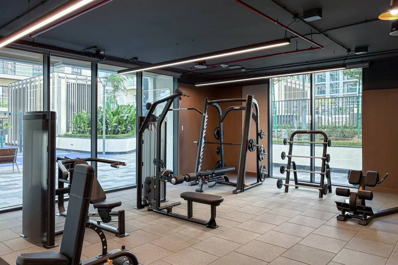 Un gimnasio con máquinas de pesas y equipo de ejercicio junto a grandes ventanales.