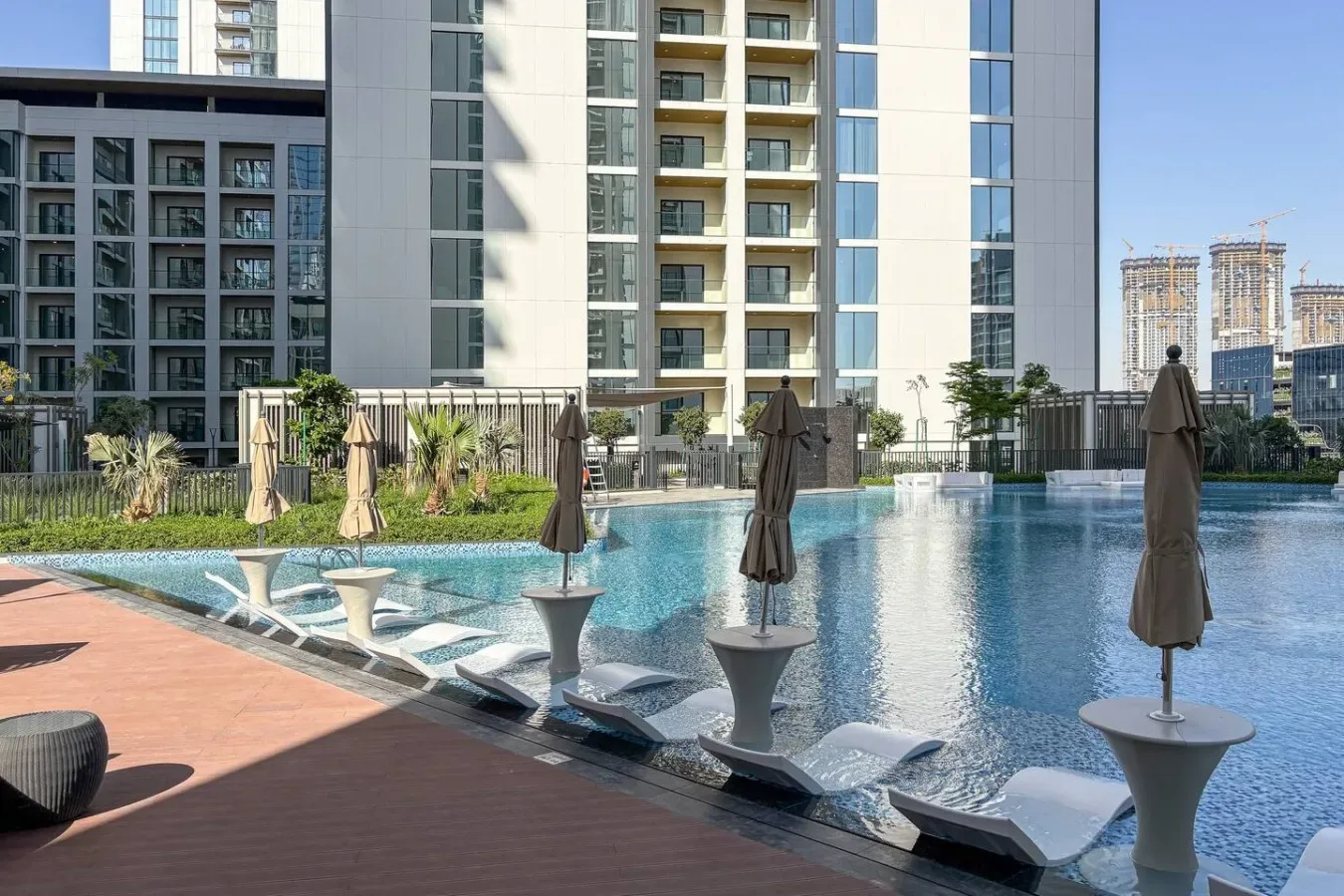 Una piscina al aire libre junto a edificios modernos, con tumbonas en el borde.