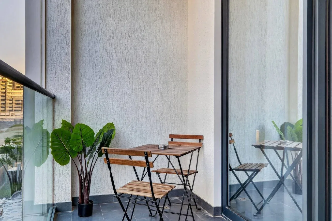 Un pequeño espacio de estar en un balcón, con una mesa plegable y sillas junto a ventanas de vidrio.