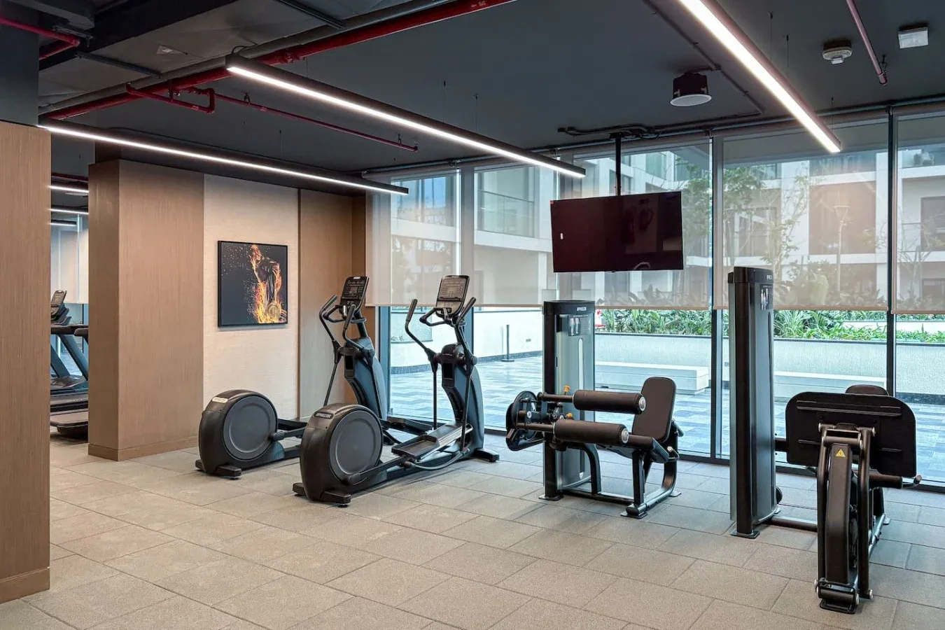 Un gimnasio con máquinas de cardio y equipos de fuerza junto a grandes ventanales.