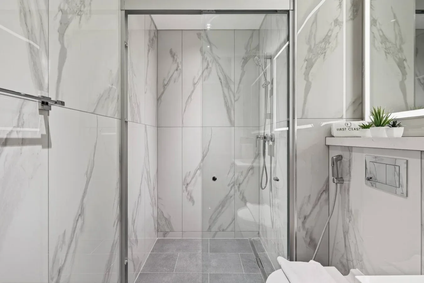 Un baño alicatado con una ducha de vidrio y una placa de descarga en la pared.