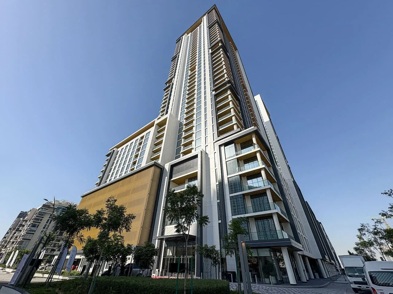 Un edificio moderno y alto se eleva sobre una entrada ajardinada bajo un cielo despejado.
