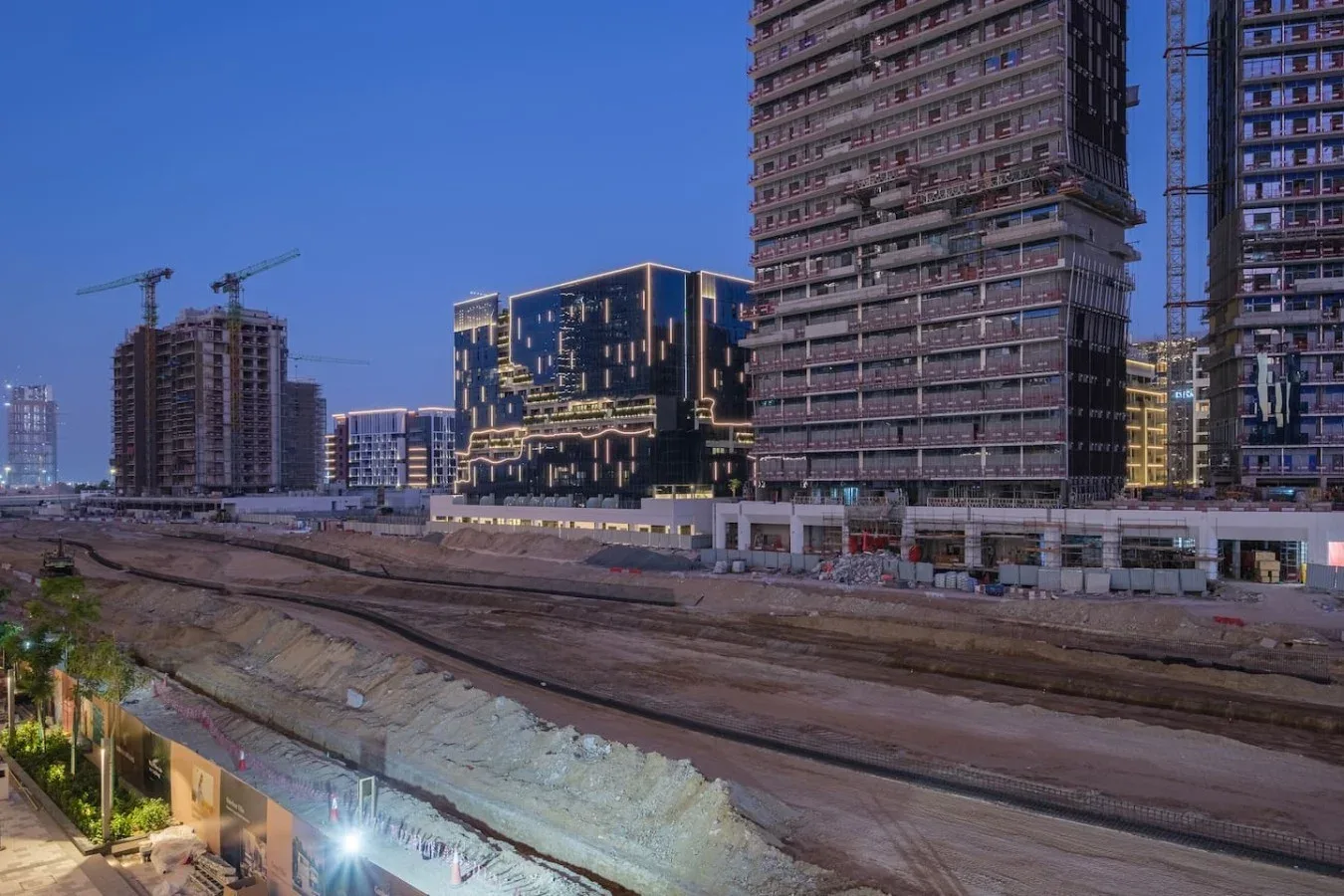 Una obra urbana con edificios altos y grúas junto a una vía excavada.