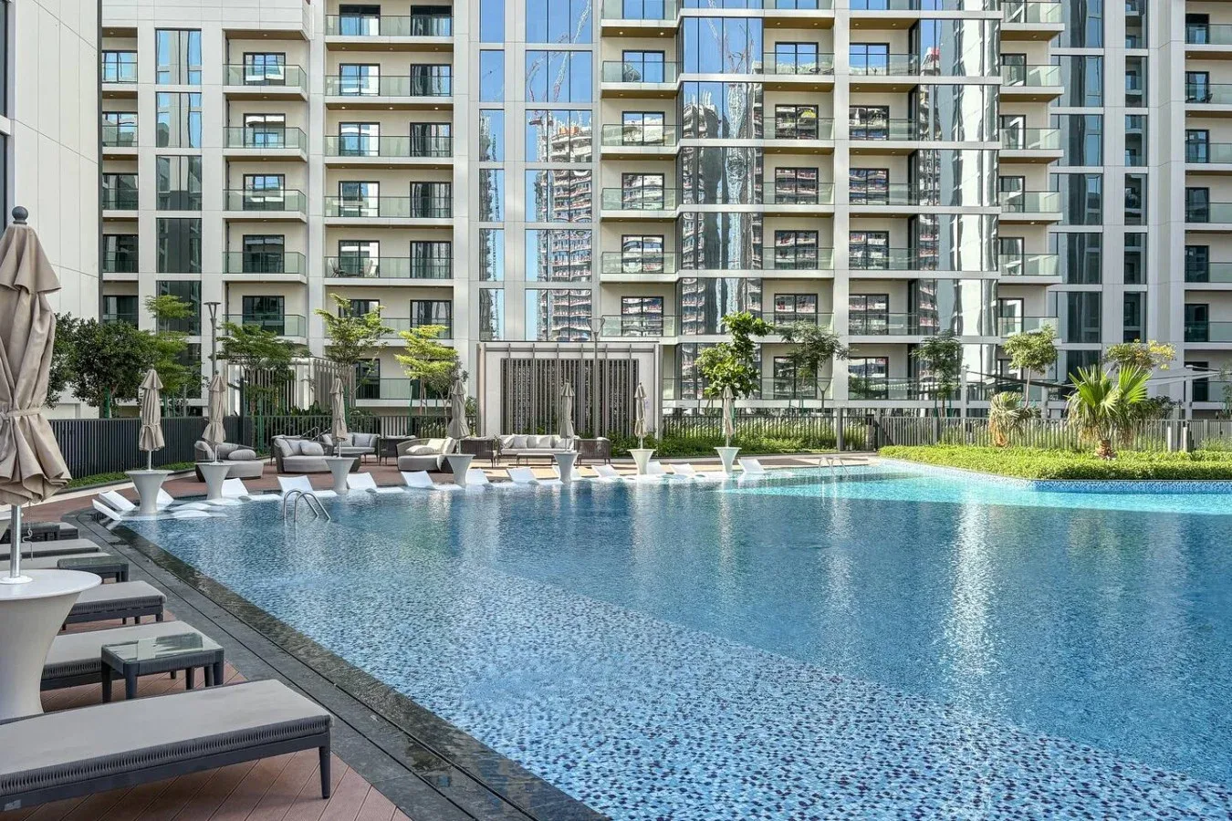 Una piscina está junto a asientos de descanso, con edificios de apartamentos al fondo.