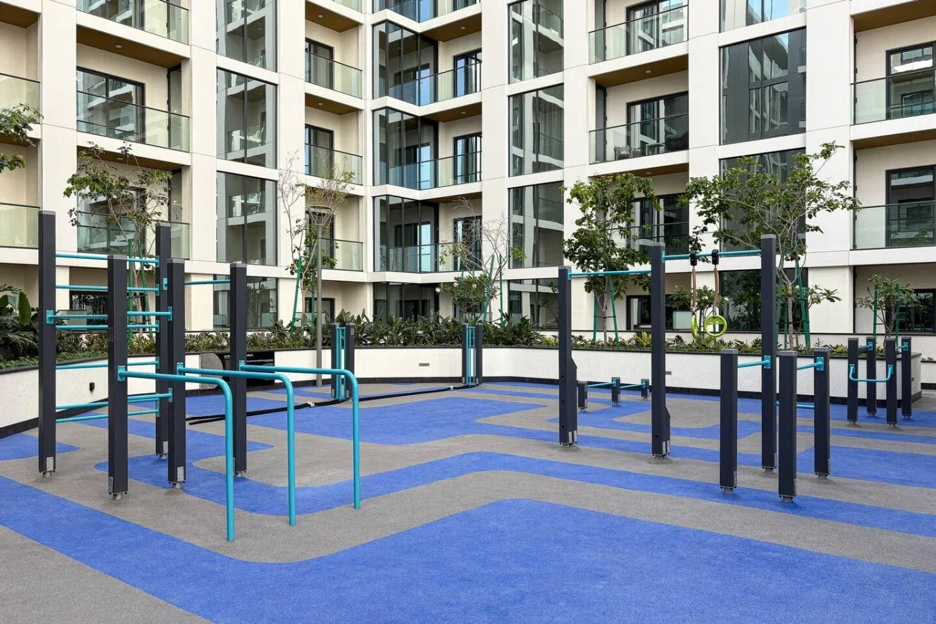 Una zona de ejercicio al aire libre con suelo azul y gris y varias estaciones de entrenamiento.