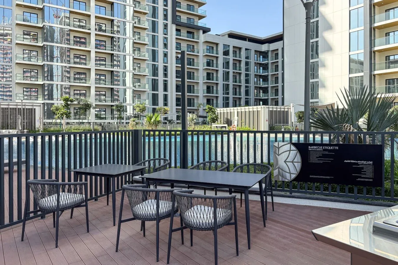 Una terraza exterior tiene mesas y asientos junto a una piscina y edificios de apartamentos.