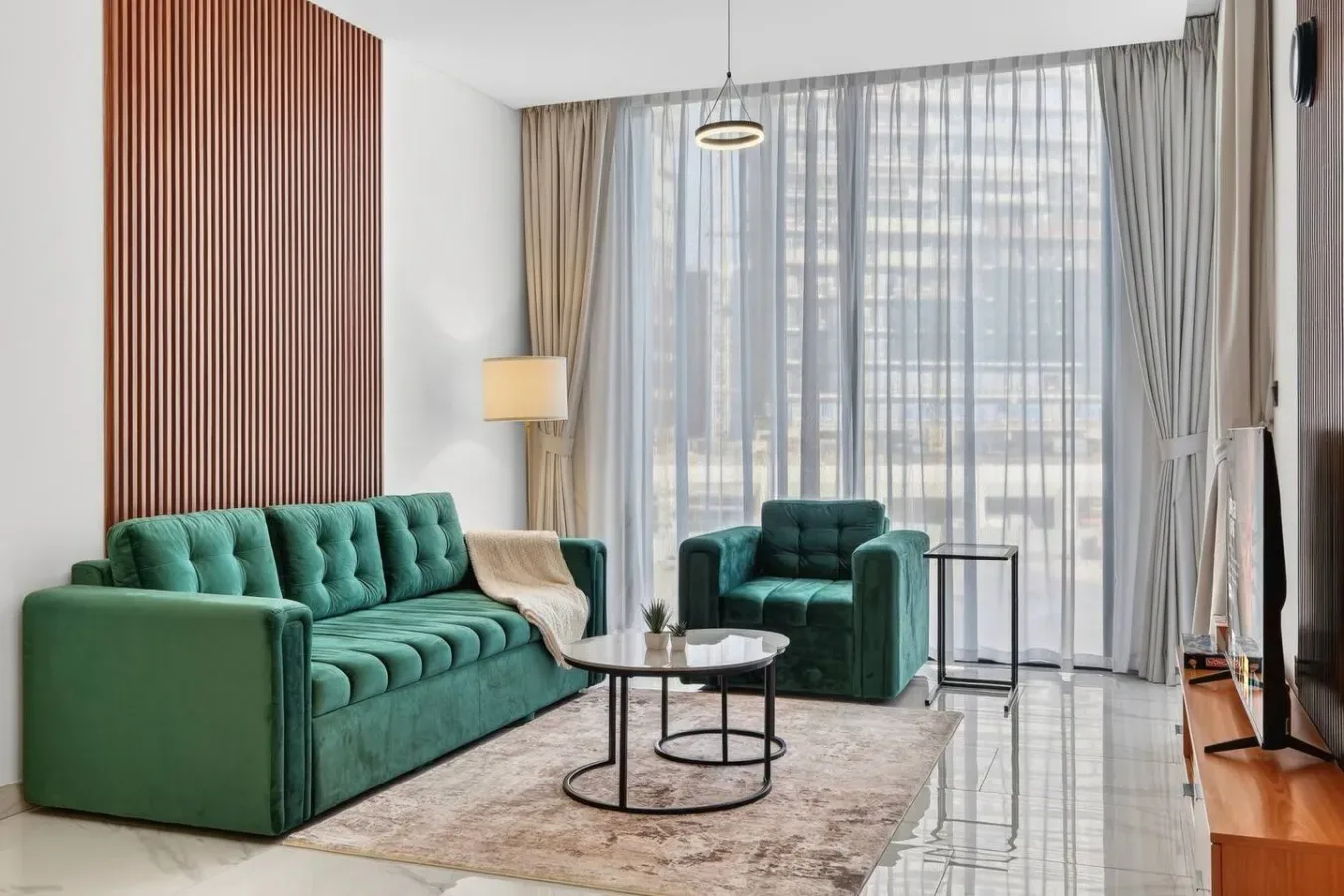 Sala de estar con asientos verdes, una mesa de centro y ventanas altas con cortinas.