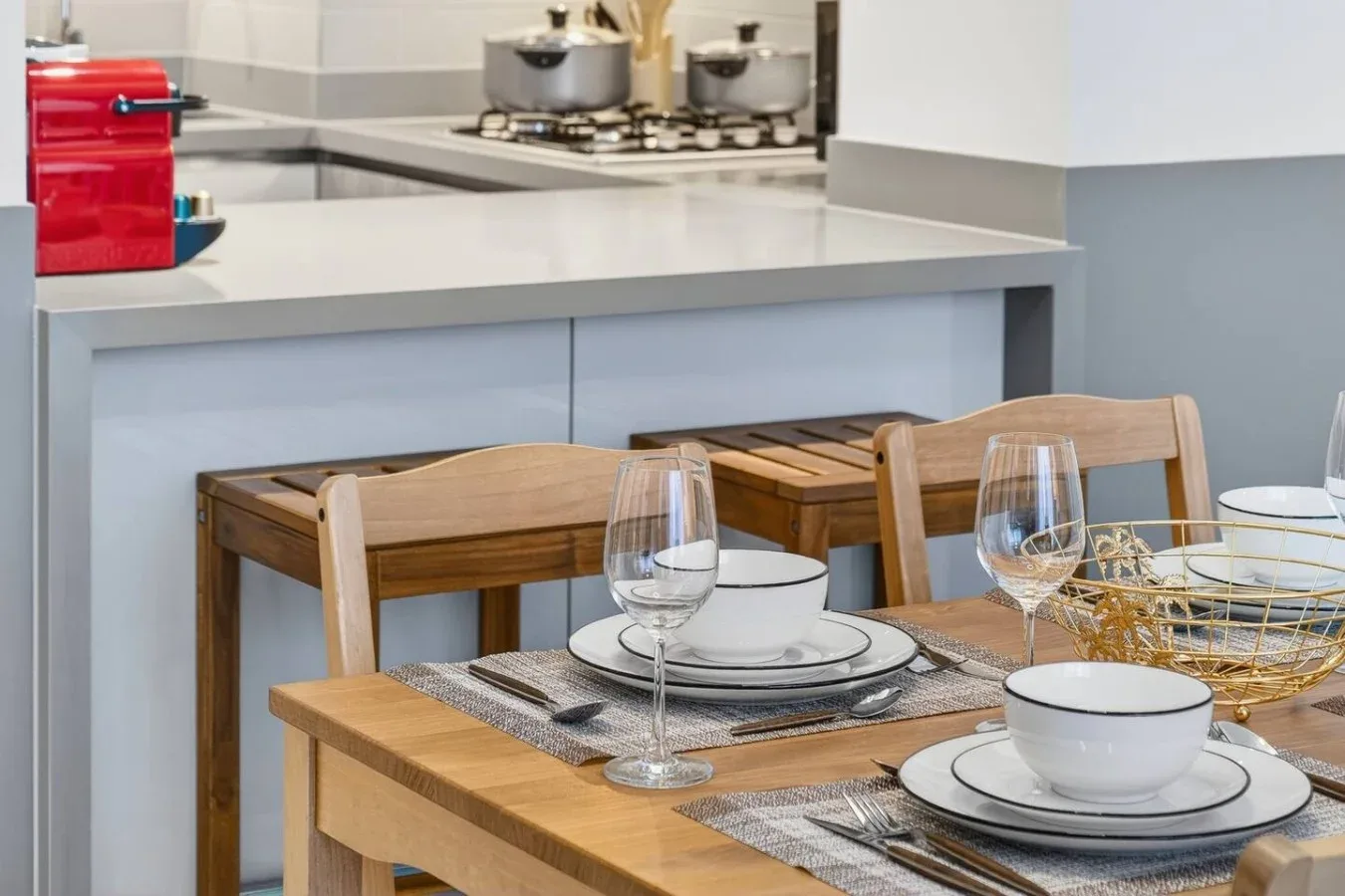 Una mesa de comedor está preparada con platos y vasos junto a una encimera de cocina.