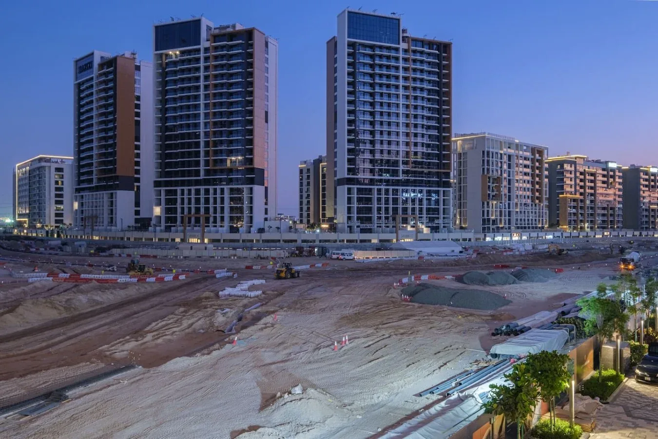 Edificios altos se alzan junto a una gran obra en construcción al anochecer.