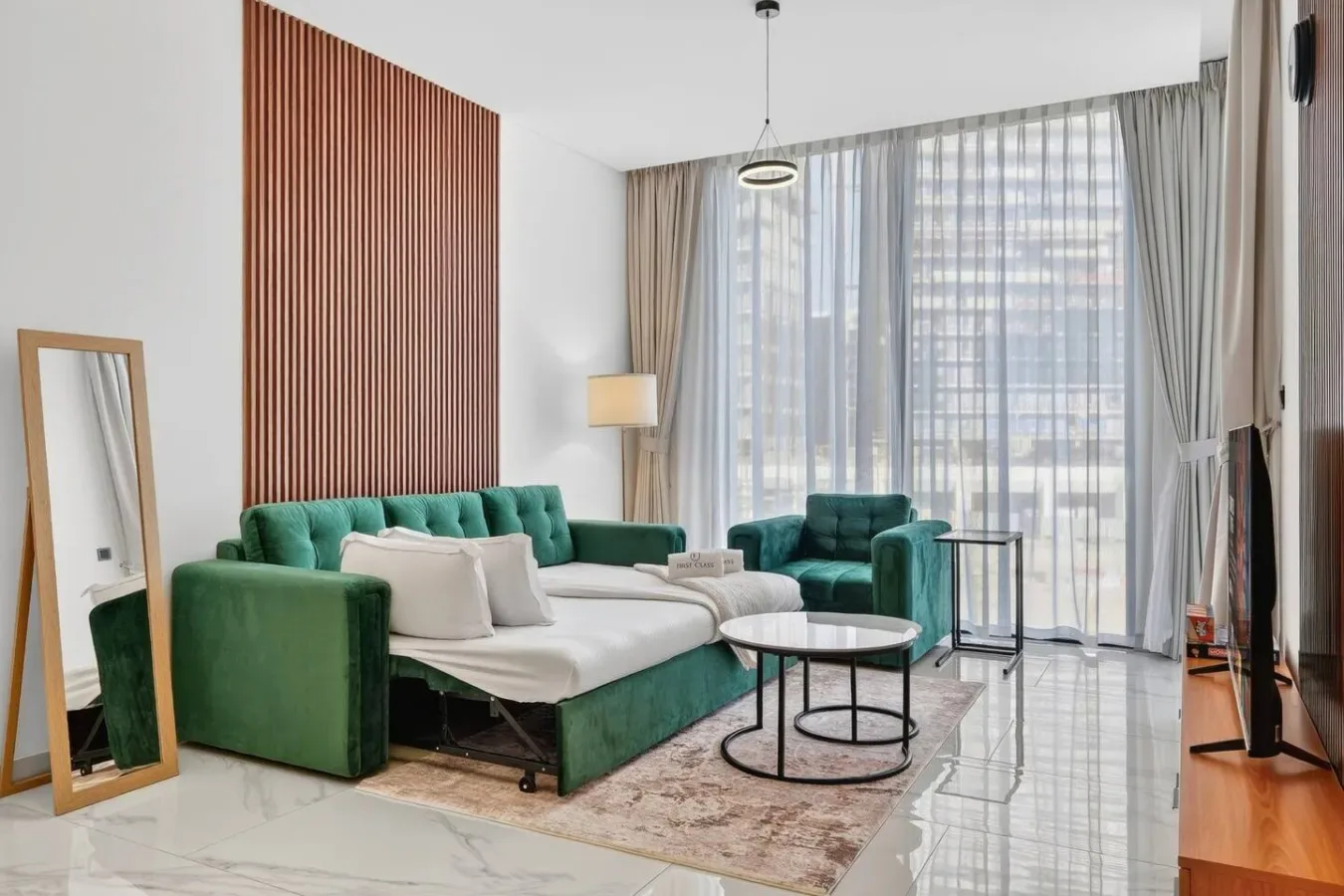 Una sala de estar con asientos verdes, una mesa de centro blanca y cortinas largas.
