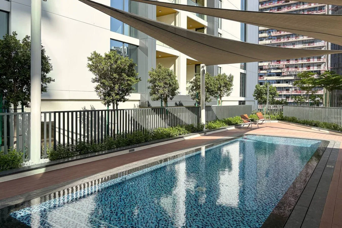 Una piscina al aire libre está junto a un edificio moderno, bajo toldos de sombra.