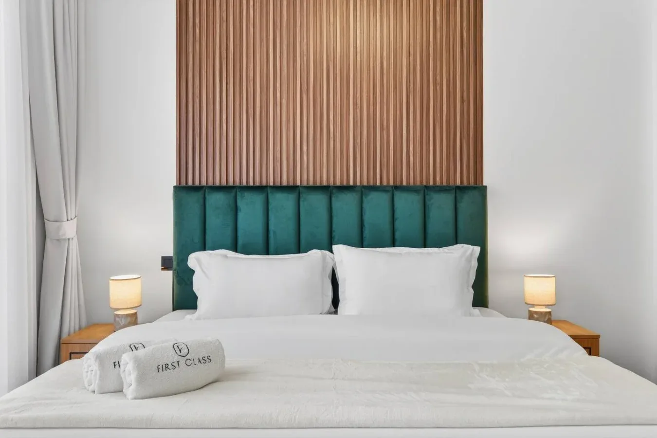 Un dormitorio ordenado con ropa de cama blanca y un cabecero tapizado de color verde azulado.