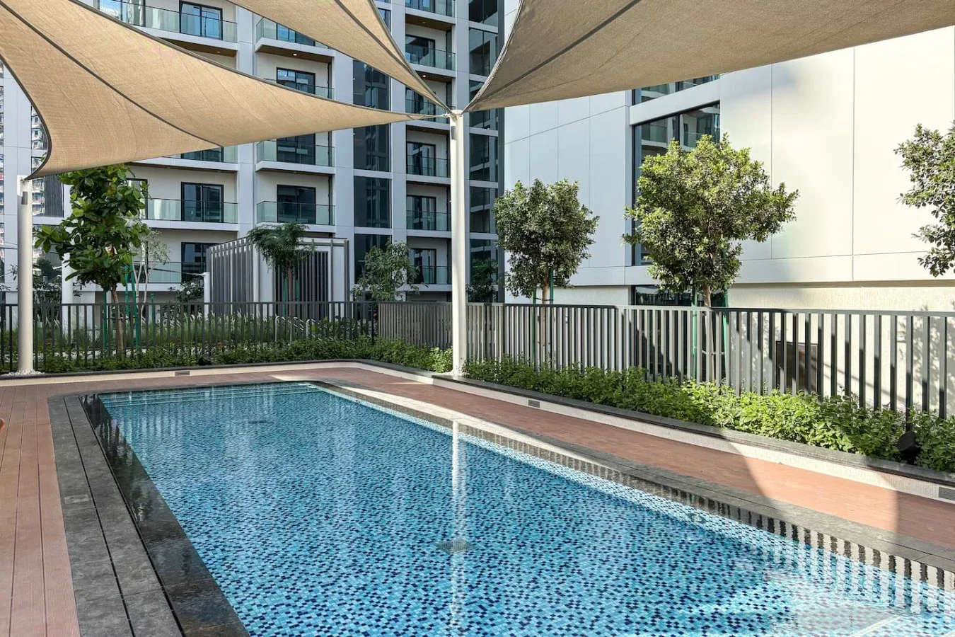 Una piscina al aire libre está bajo velas de sombra junto a un patio ajardinado.