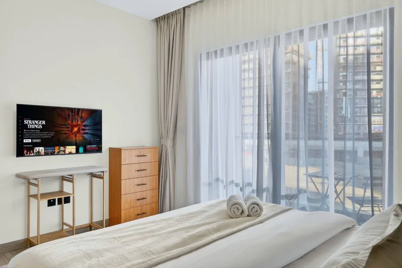 Un dormitorio con una cama, un televisor y cortinas translúcidas sobre una ventana amplia.